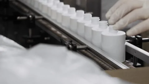 A worker in a cosmetics factory places empty plastic bottles on a conveyor. Stock Footage 306576606