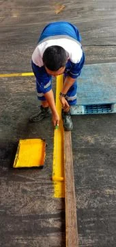 A worker creates a boundary line using a yellow paint roller brush. Stock-Fotos