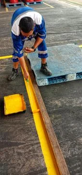 A worker creates a boundary line using a yellow paint roller brush. Photos