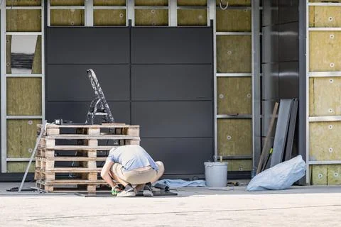 A worker is crouched down, inspecting materials on wooden pallets at a cons.. Stock Photos