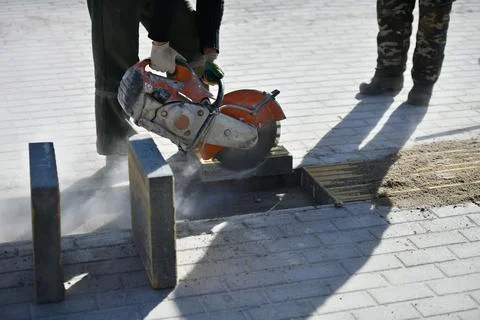 A worker cuts with a circular saw, construction work on a city street. Stock Photos