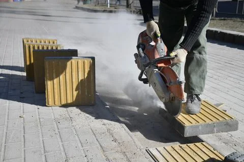 A worker cuts with a circular saw, construction work on a city street. Stock Photos