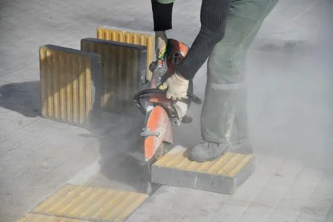 A worker cuts a curb stone with a circular saw on a construction site. Stock Photos