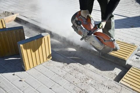 A worker cuts curbstone with a circular saw at a construction site. Stock Photos