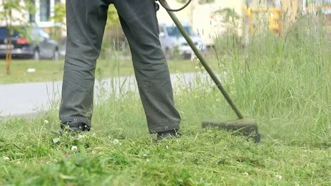 The worker cuts the grass with lawn string trimmer Stock Footage