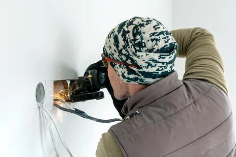 Worker cuts a hole in the wall. Installing new outlets. Work with an electric Stock Photos