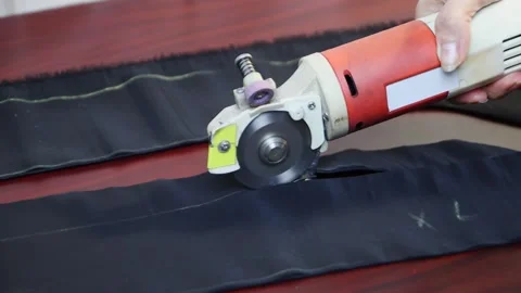 Worker cuts layers of dark tissue with electric cutter on a brown table. FullHD Vídeos de archivo 141121318