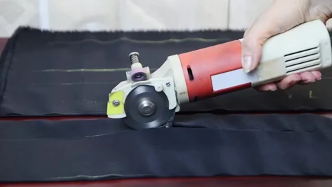Worker cuts layers of dark tissue with electric cutter on a brown table. FullHD Vídeo Stock 141239311