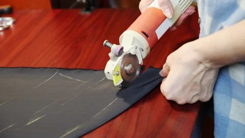 Worker cuts layers of dark tissue with electric cutter on a brown table. FullHD Vídeo Stock 141314378