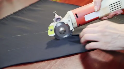 Worker cuts layers of dark tissue with electric cutter on a brown table. FullHD Vídeo Stock 141429629