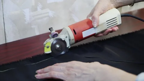 Worker cuts layers of dark tissue with electric cutter on a brown table. FullHD Vídeo Stock 141502081