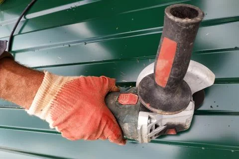 Worker cuts a metal sheet with an angle grinder outdoors in the village. Fotos de archivo