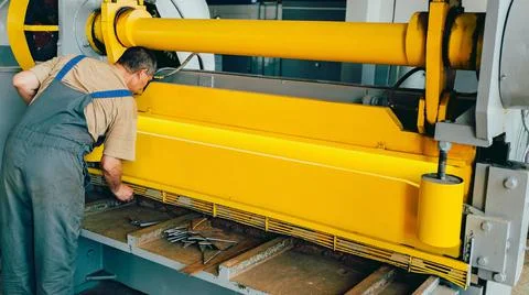 Worker cuts metal sheets on mechanical guillotine machine in production hall. Stock Photos