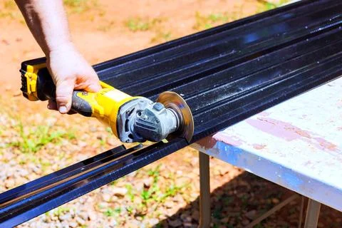 Worker cuts metal track using power tool at construction workshop Stock Photos