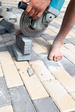 A worker cuts paving slabs with a grinder for subsequent laying, vertical sho Stock Photos