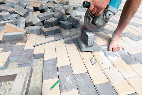 A worker cuts paving slabs with a grinder for subsequent laying. Stock Photos