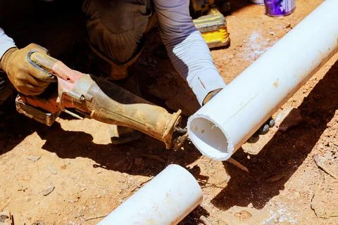 Worker cuts plastic pipe to waste drain in construction area Stock Photos