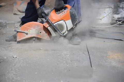 A worker cuts the road surface with a circular saw . Stock Photos