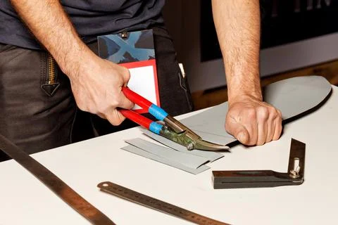 A worker cuts a sheet of roofing iron with metal scissors. Stock Photos