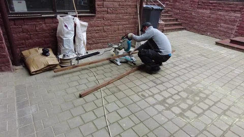 Worker cuts wood on a saw in a backyard at a construction site during daytime Stock Footage 340357197