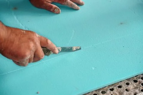 Worker cutting blue polystyrene foam heat insulation with old retractable u.. Stock Photos