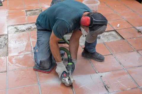 Worker cutting ceramic floor tiles with angle grinder during renovation Stock Photos