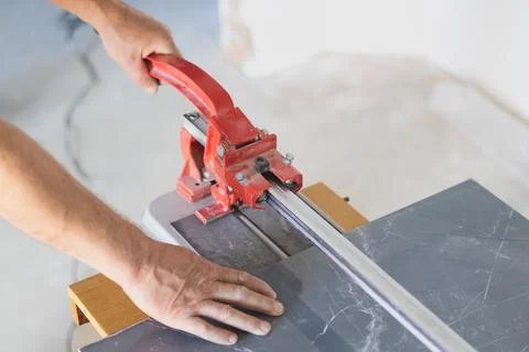 A worker is cutting a ceramic tile on a special cutter saw machine. Stock Photos