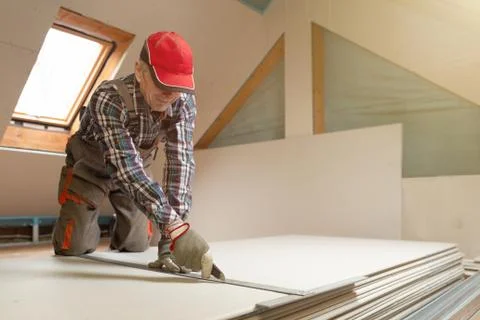 Worker cutting drywall plasterboard with construction knife. Attic renovation Stock Photos