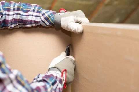 Worker cutting drywall plasterboard with construction knife. Attic renovation Stock Photos