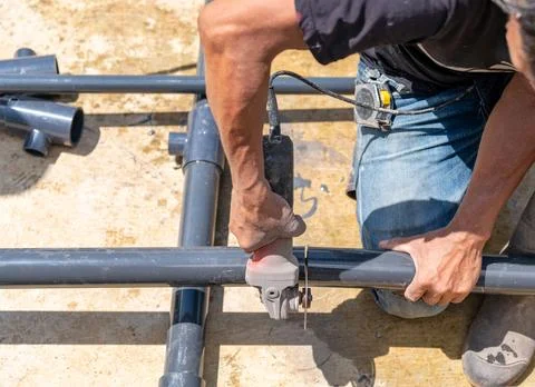 Worker cutting grey pipe with electric disk blade grind. Stock Photos