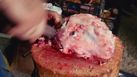 A worker cutting with a large knife the outer flesh of the skull of a pig Stock Footage 165539326