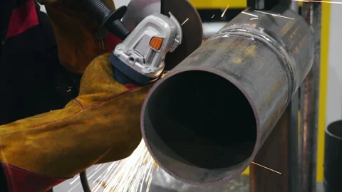 Worker cutting metal pipe with angle grinder in workshop. Stock Footage 347786979