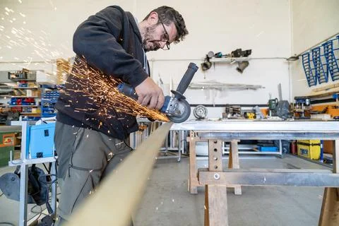 Worker cutting metal profile with angle grinder producing sparks Stock Photos
