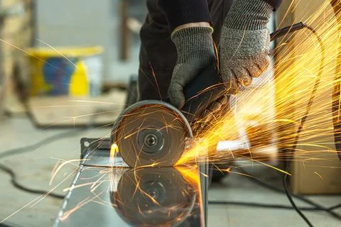 A worker cutting a square galvanized ventilation pipe with an angle grinder Stock Photos