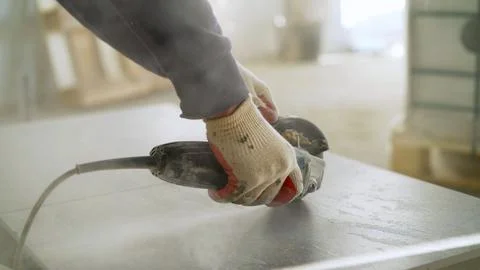 Worker cutting stone tile with angle grinder creating dust in a workshop Fotos de archivo