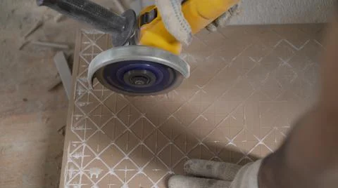 Worker cutting a tile using an angle grinder at construction site. A worker is Stock Photos