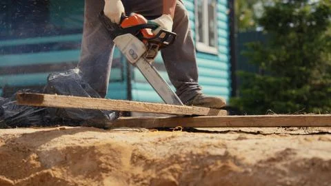 Worker cutting wood plank using a power chainsaw Stock Photos