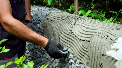 A worker decorates a wall in the garden, lays granite rubble on tile adhesive. Stock Footage 206823988