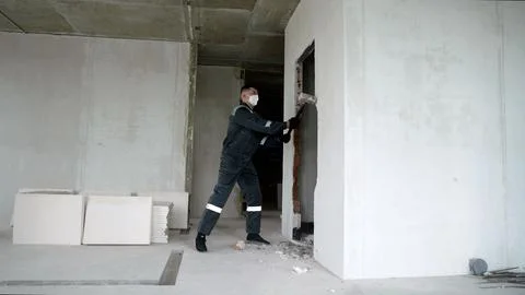 Worker demolishing interior brick wall with sledgehammer at construction site Stock Photos