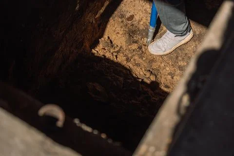 Worker digging and cleaning soil in vehicle service pit inside garage 库存照片