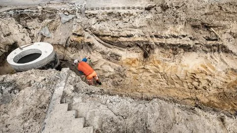A worker is digging in a deep pit to construct a concrete sewer well. The are Stock Photos