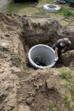 A worker digs and prepares to place a large concrete pipe into a trench at a  Stock Photos