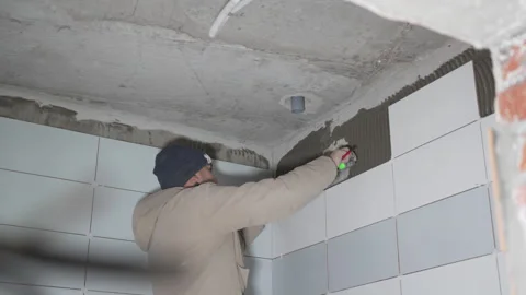 Worker diligently tiles walls with ceramic tiles in building Stockbeeldmateriaal 306417711