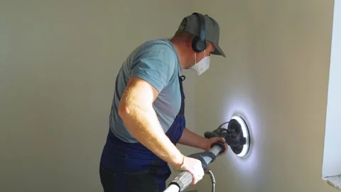 Worker diligently works inside house on sunny day. Leveling and sanding walls Stock Footage 319210497