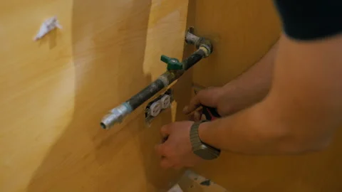 Worker disconnecting plumbing and electrical outlet under a kitchen cabinet Stock Footage 332185558