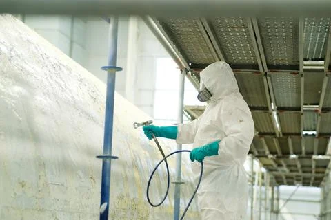 A worker dressed in a full protective suit and mask is spray painting a large Foto stock