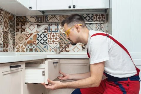 Worker dressed in workers' overall assembing furniture in kitchen Stock Photos