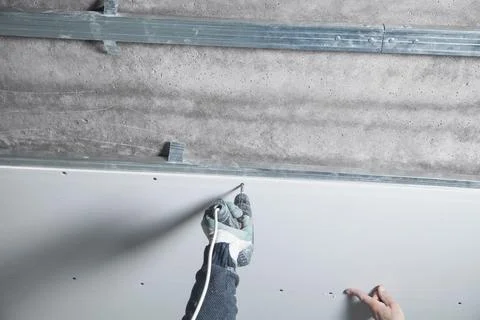 Worker with a drill screwdriver twists the screw into the drywall. Stock Photos