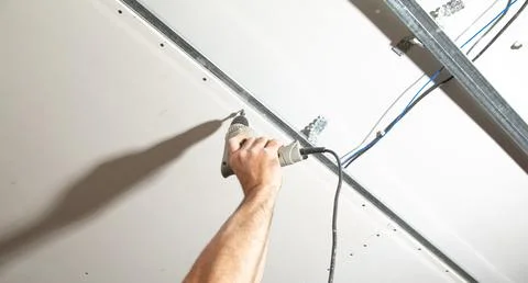 Worker with a drill screwdriver twists the screw into the drywall. Stock Photos