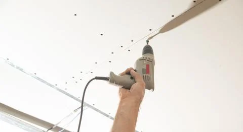 Worker with a drill screwdriver twists the screw into the drywall. Stock Photos